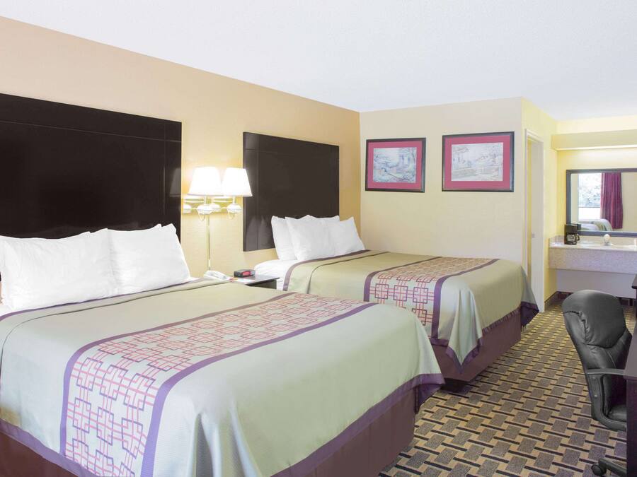 A hotel room with two beds, a desk, a chair, a lamp, and a mirror.