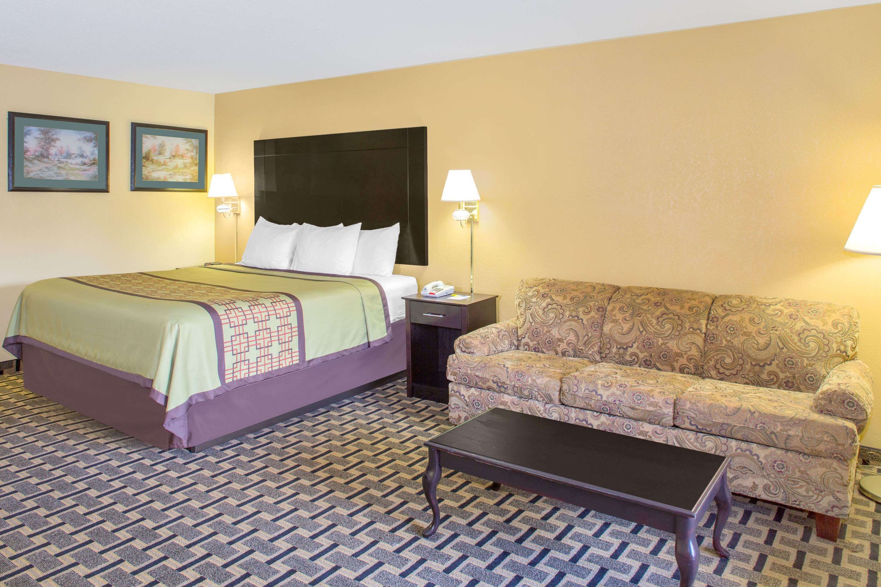 Una habitación de hotel con una cama, un sofá, una mesa de centro y dos lámparas fijadas a la pared.