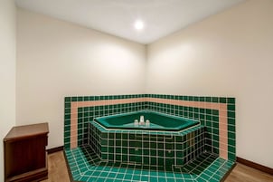 Una bañera de esquina con azulejos verdes y un banco de madera.