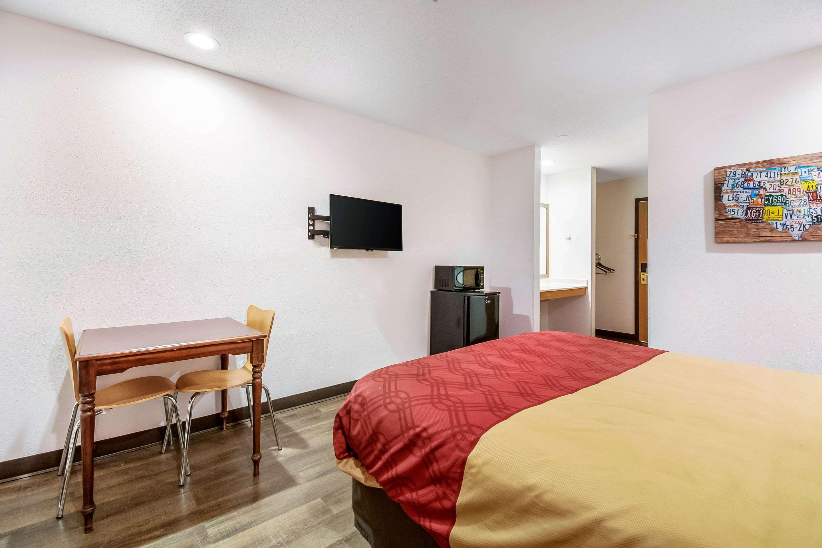 A hotel room with a bed, a desk with a chair, a television mounted on the wall, and a door leading to a bathroom.