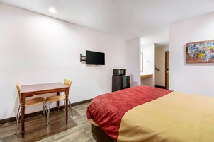 Habitación de hotel con cama, escritorio con silla, televisor montado en la pared y puerta que da a un baño.