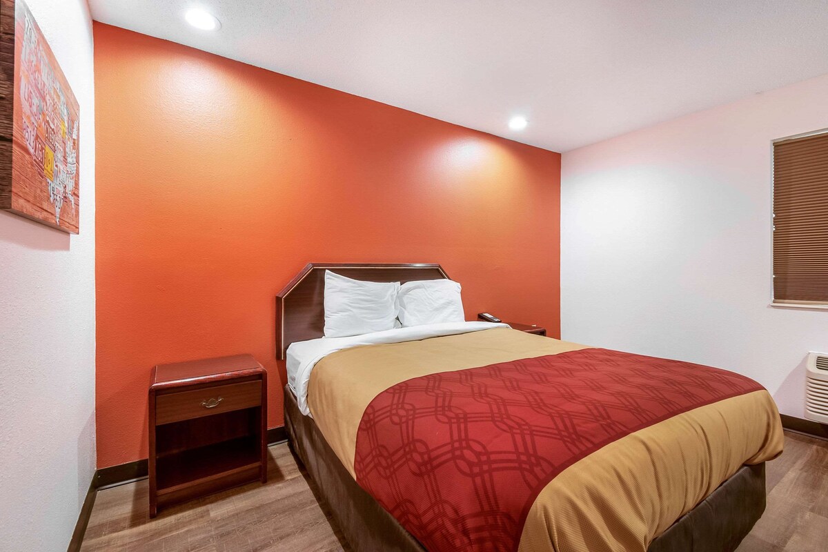 Une chambre d’hôtel avec un lit, une table de chevet, un radiateur fixé au mur et un tableau accroché au mur.
