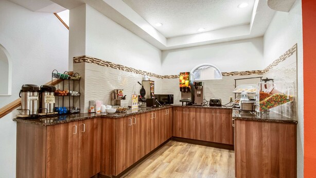 Una cocina moderna con armarios de madera, microondas, cafetera y una exposición de frutas.