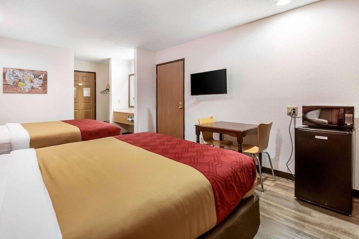Habitación de hotel con dos camas, un escritorio, una silla, un televisor y un refrigerador.