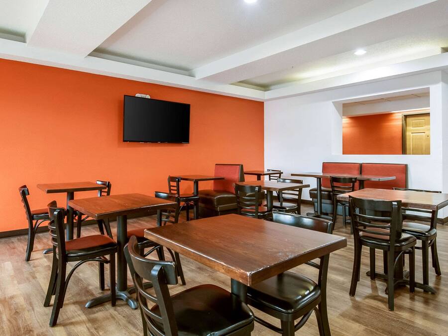 A restaurant interior with multiple tables and chairs, a flat-screen TV mounted on the wall, and a wooden floor.