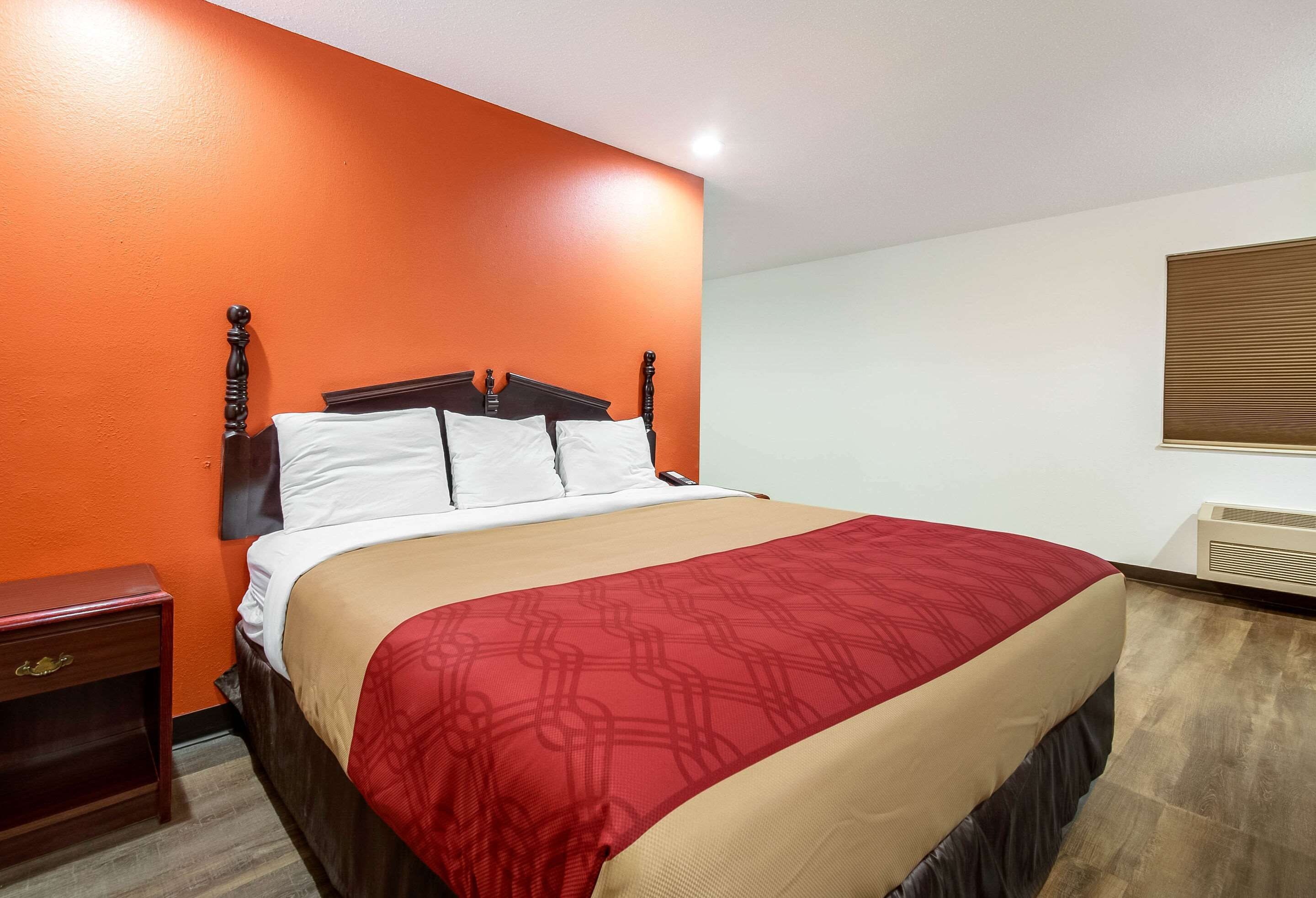 A hotel room with a bed, a nightstand, a dresser, and a window with blinds.