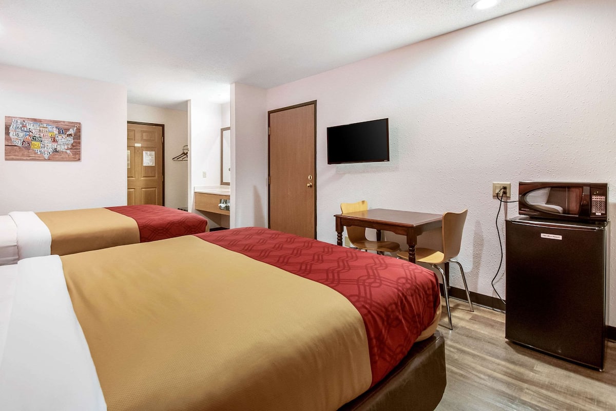 Habitación de hotel con dos camas, un escritorio, una silla, un televisor y un refrigerador.