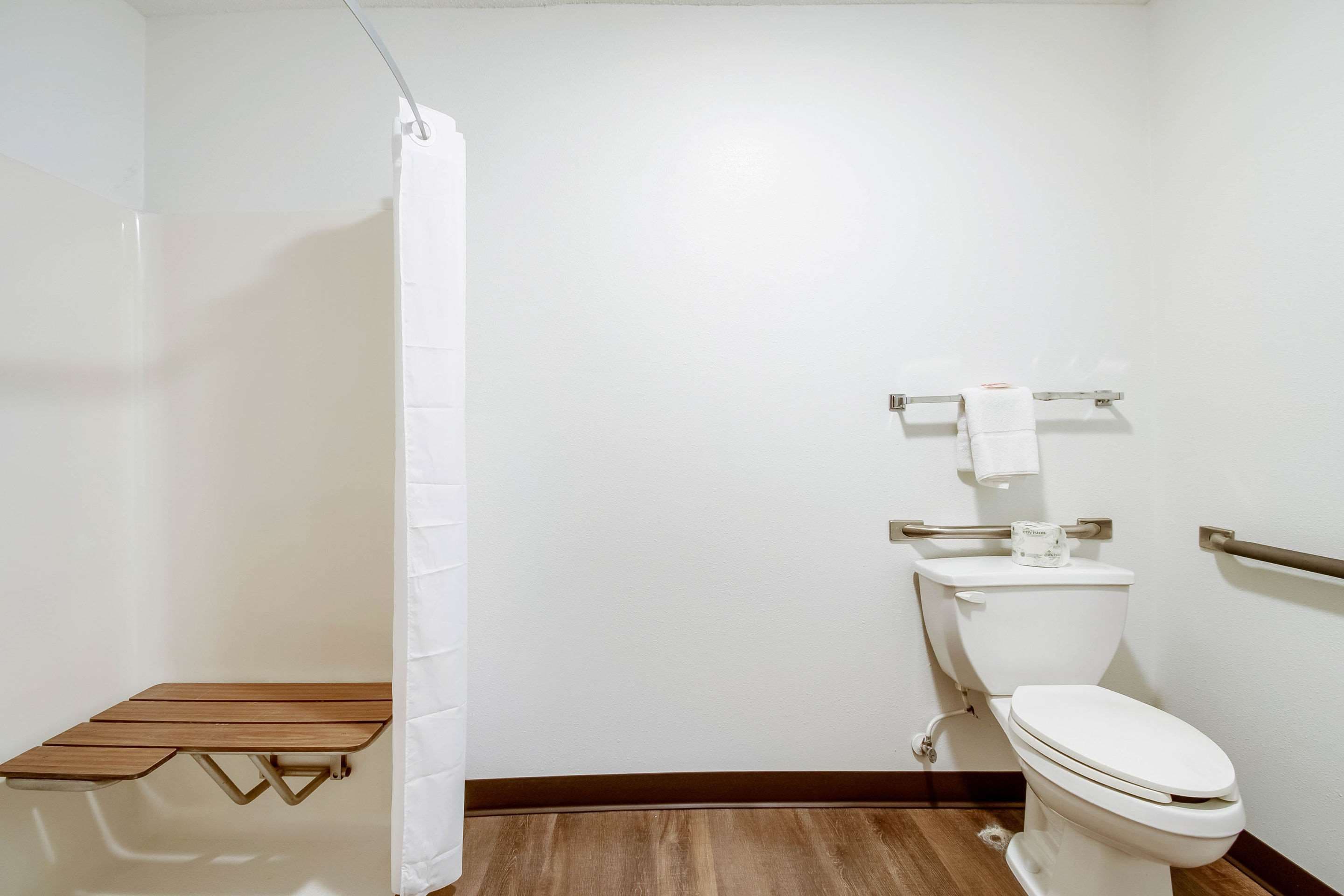 A small bathroom with a toilet, a shower curtain, and a wooden bench.