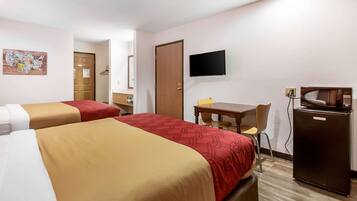 A hotel room with two beds, a desk, a television, and a refrigerator.