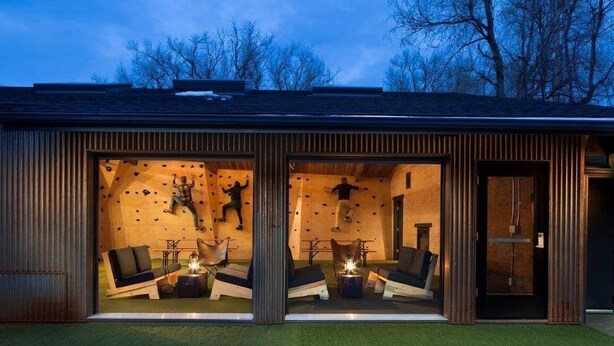 A modern building with large glass windows, a rock climbing wall, and outdoor seating. - Basecamp Boulder (Boulder)