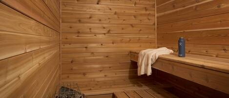 A sauna with wooden walls and benches, a metal container with rocks, and a water bottle on a bench.
