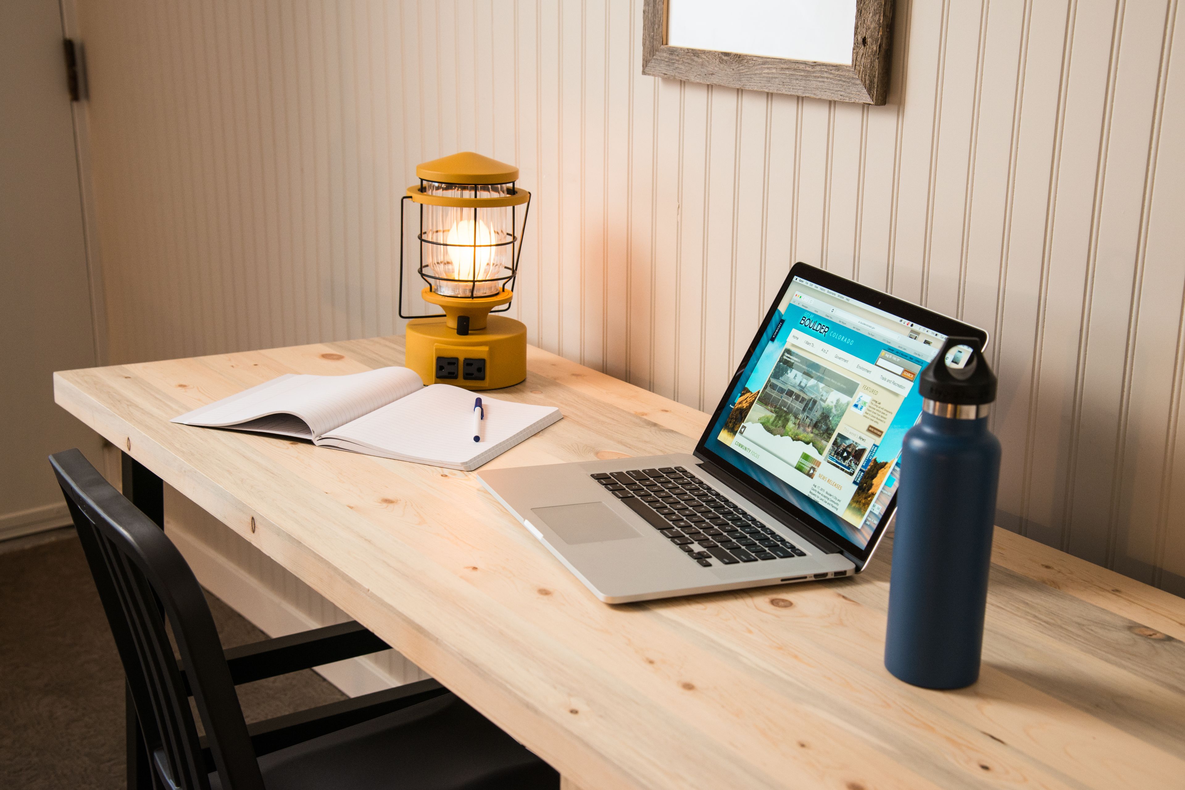 A wooden desk with a laptop, a notebook, a pen, and a yellow lamp.