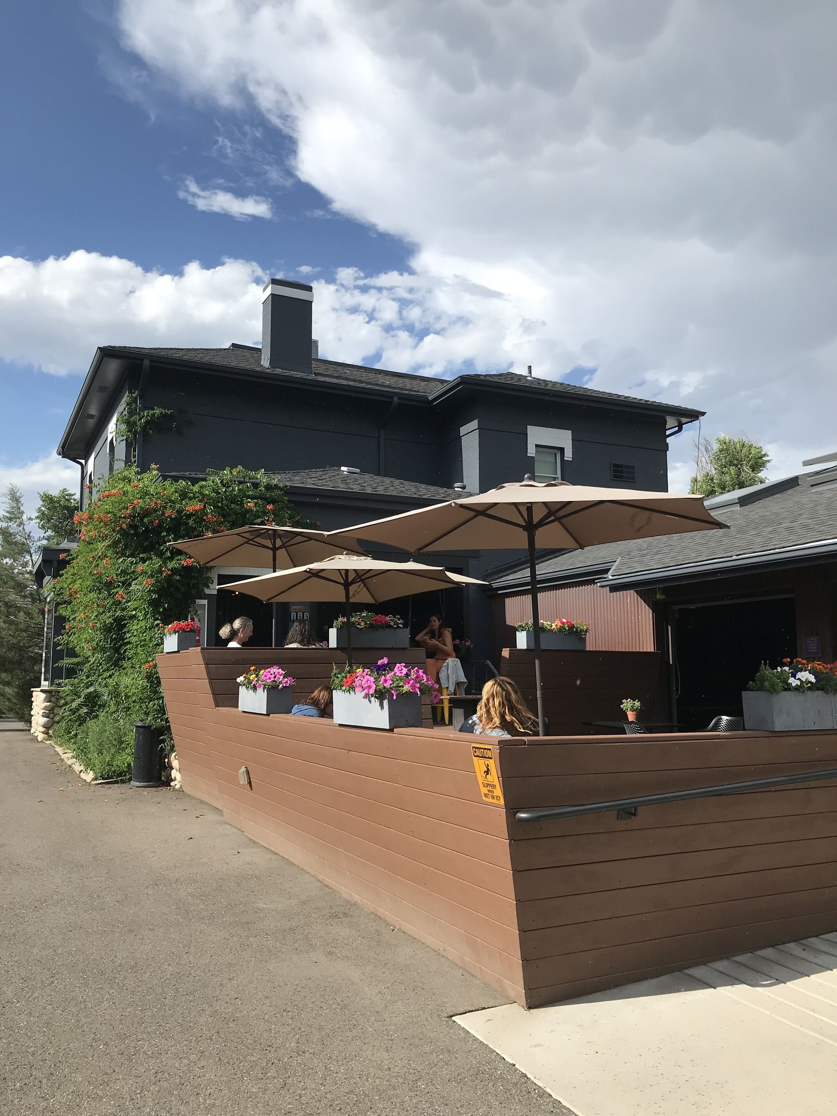 Un espace extérieur aménagé avec des tables et des parasols, entouré de jardinières fleuries.