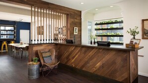 A reception area with a wooden reception desk, a seating area with chairs, a dining table, and a view of a green wall with plants. - Basecamp Boulder (Boulder)