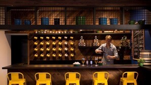A bar area with a bartender, yellow stools, and a wall of liquor bottles. - Basecamp Boulder (Boulder)