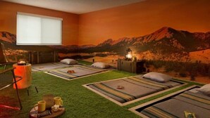 A room with four beds, a massage table, a window, and a mural of mountains. - Basecamp Boulder (Boulder)