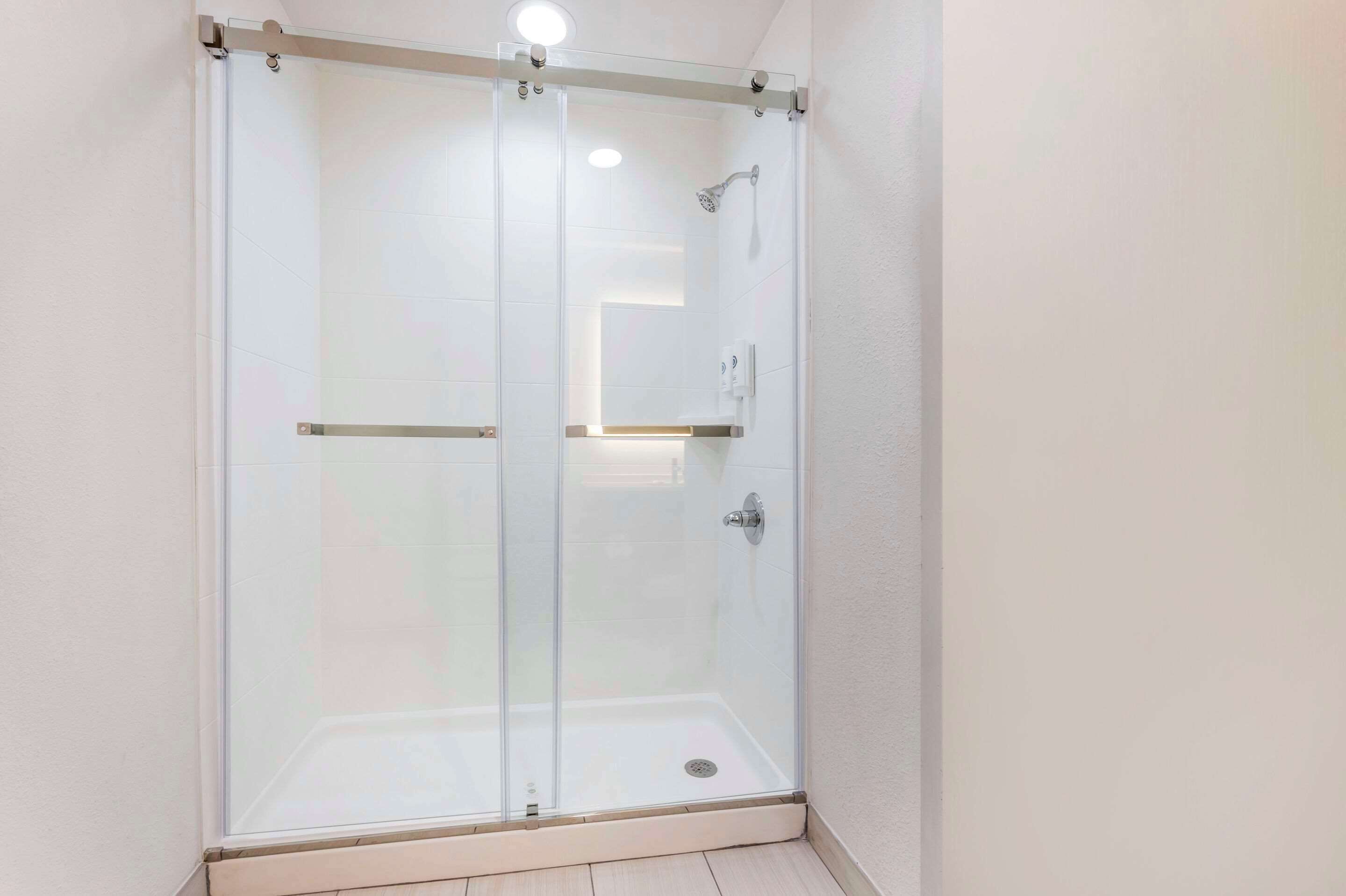 A glass-enclosed shower area with a showerhead and a control panel.