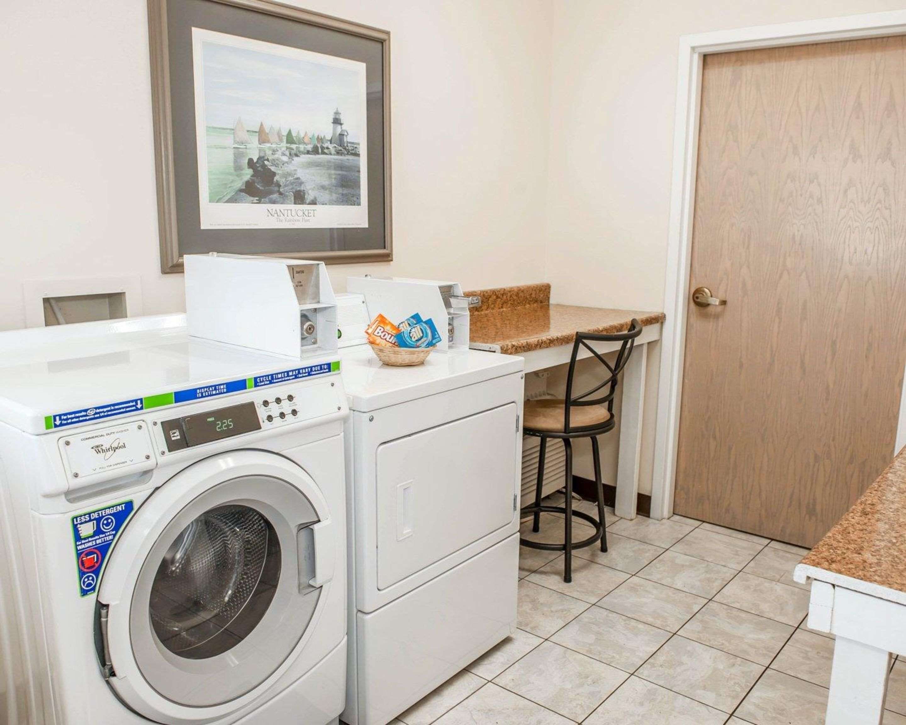 A laundry area with a Whirlpool washer and dryer, a small table with a basket of detergent, and a framed picture of Nantucket on the wall.