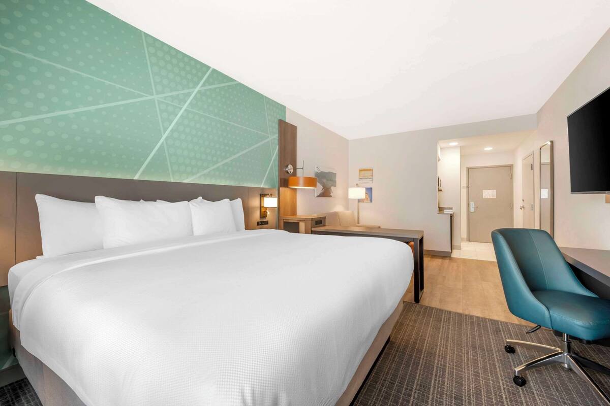 A hotel room with a large bed, a desk, a chair, and a TV.