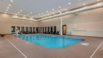 An indoor swimming pool with clear water, surrounded by lounge chairs and a tiled floor.