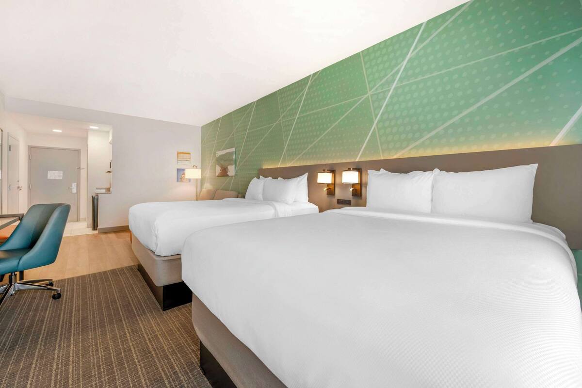 A hotel room with two beds, a desk, and a chair.