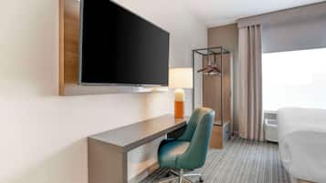 Hotelkamer met een groot flatscreen televisietoestel aan de muur, een bureau met stoel, een nachtkastje met lamp, een bed en een raam met gordijnen.