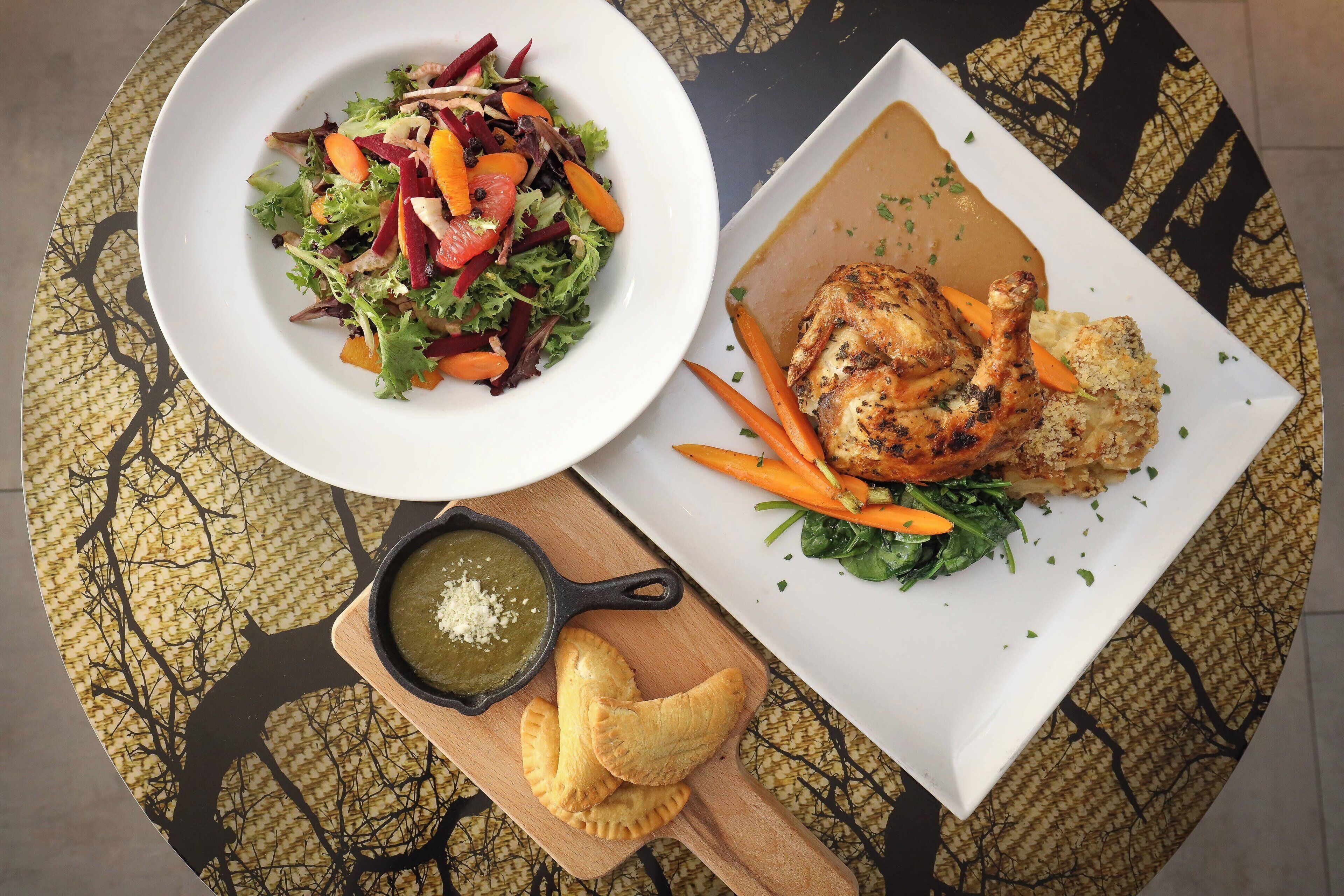 A table with a plate of roasted chicken, a salad, and a bowl of green sauce.