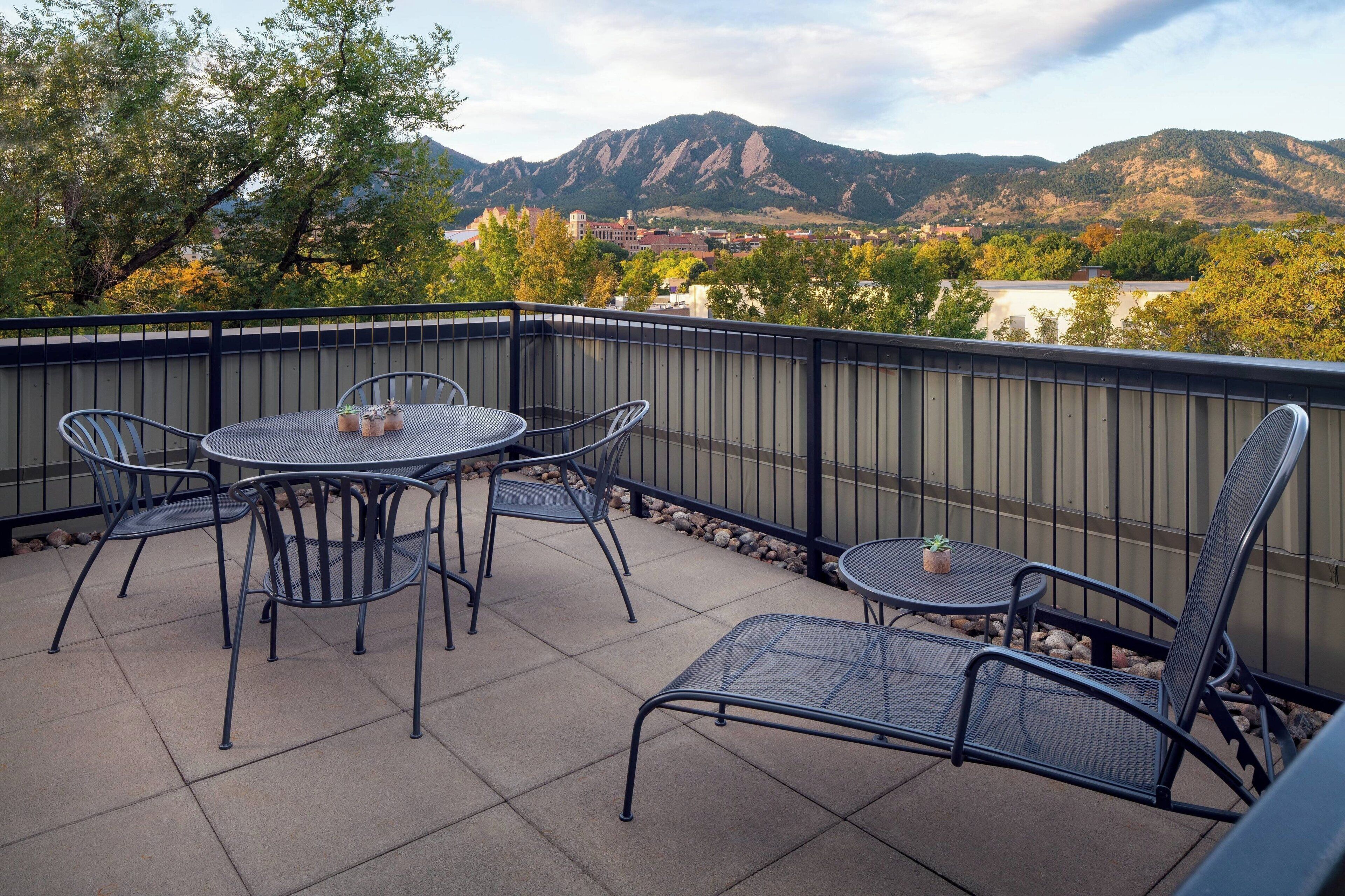 A balcony with a table and chairs, a view of mountains, and a fence.