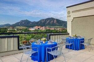 A terrace with tables set for dining, overlooking a mountainous landscape and a historic building.