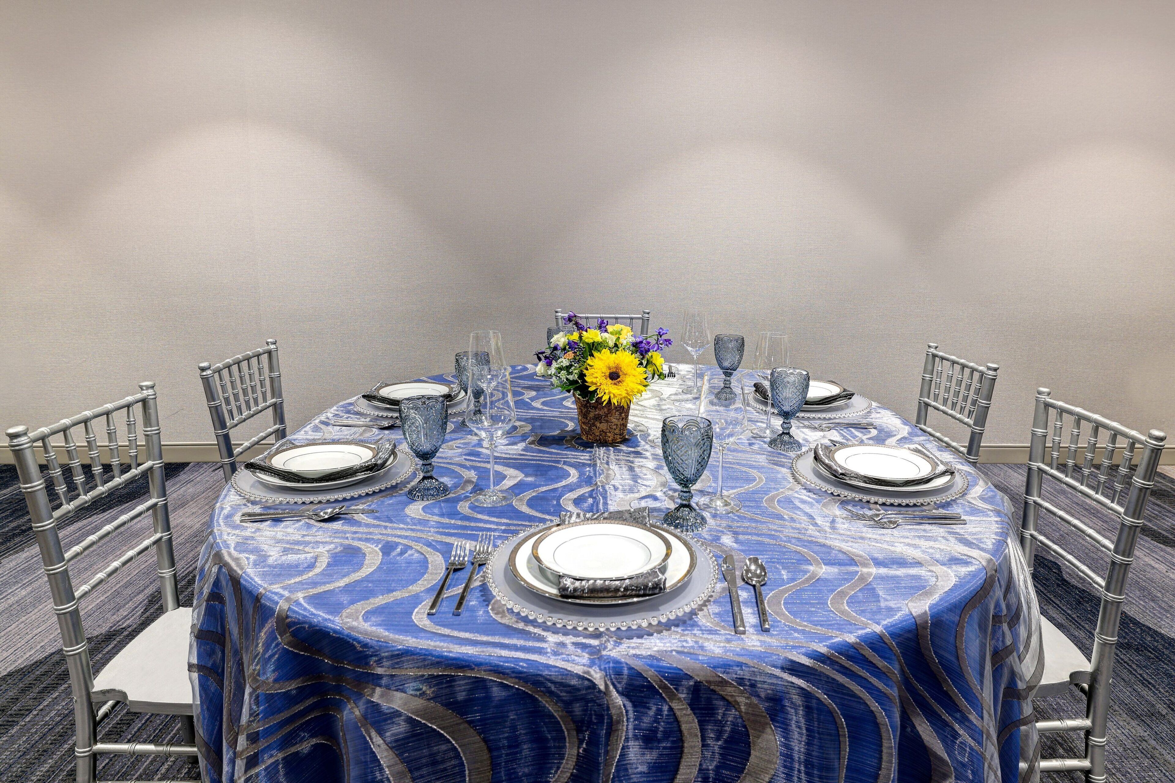 A round table with a blue patterned tablecloth, surrounded by metal chairs.