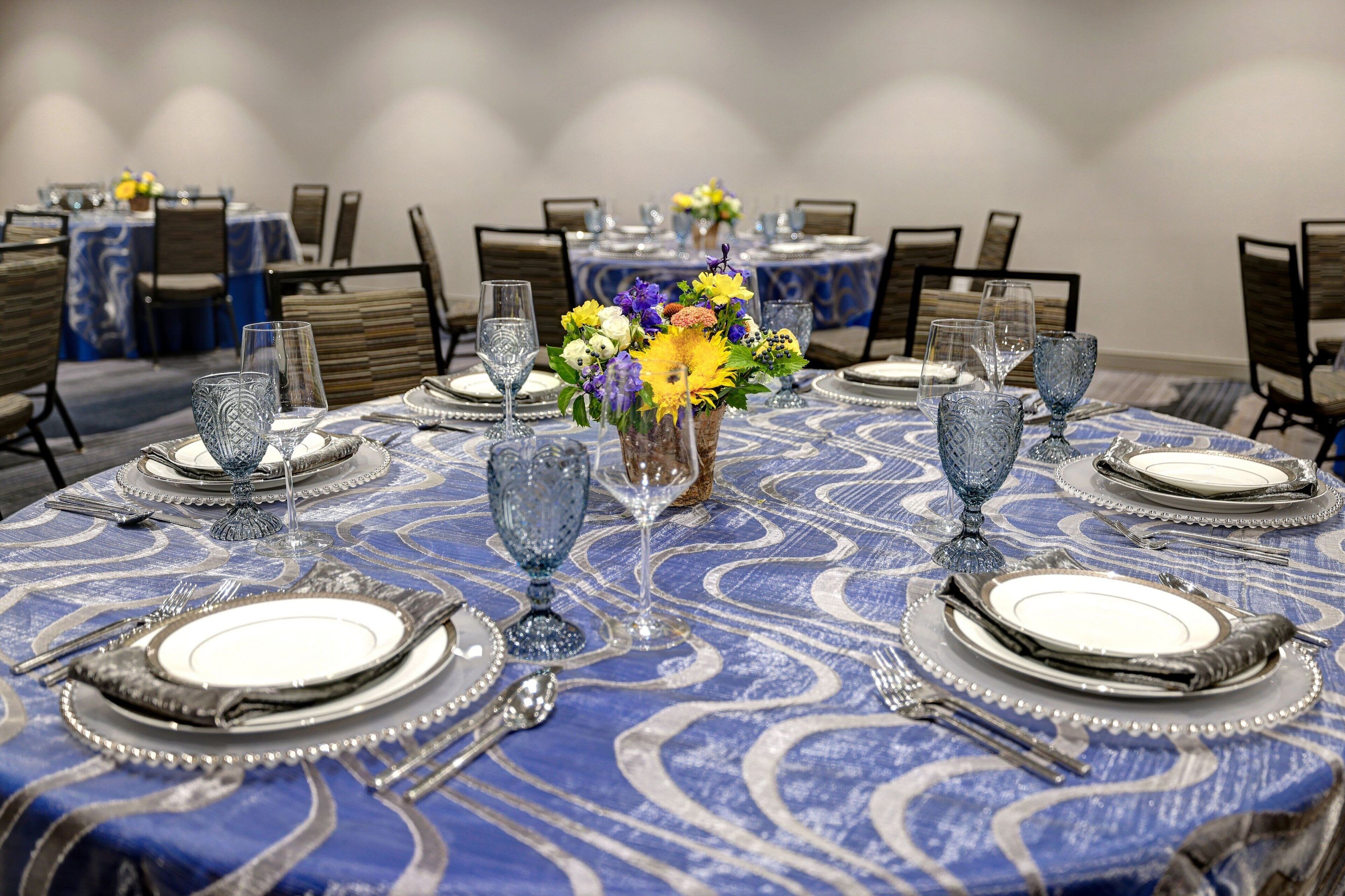 A dining area with round tables set for a meal, featuring blue tablecloths and silverware.