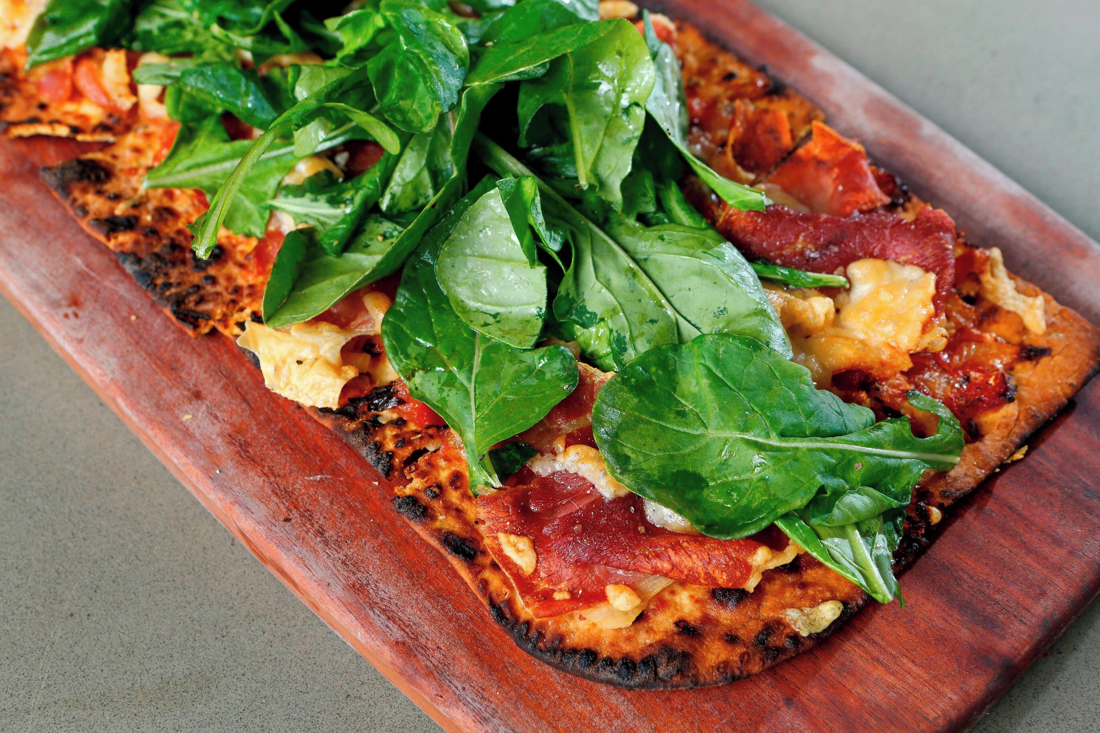 Pizza con espinacas y tocino sobre una tabla de madera.