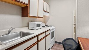 A compact kitchen with white cabinets, a stainless steel sink, a microwave, a stove, and a refrigerator. - Extended Stay America Suites Fort Wayne North (Fort Wayne)