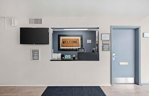 A reception desk with a 'WELCOME' sign, a flat-screen TV, a digital kiosk, and a door with a sign indicating office hours. - Extended Stay America Suites Fort Wayne North (Fort Wayne)