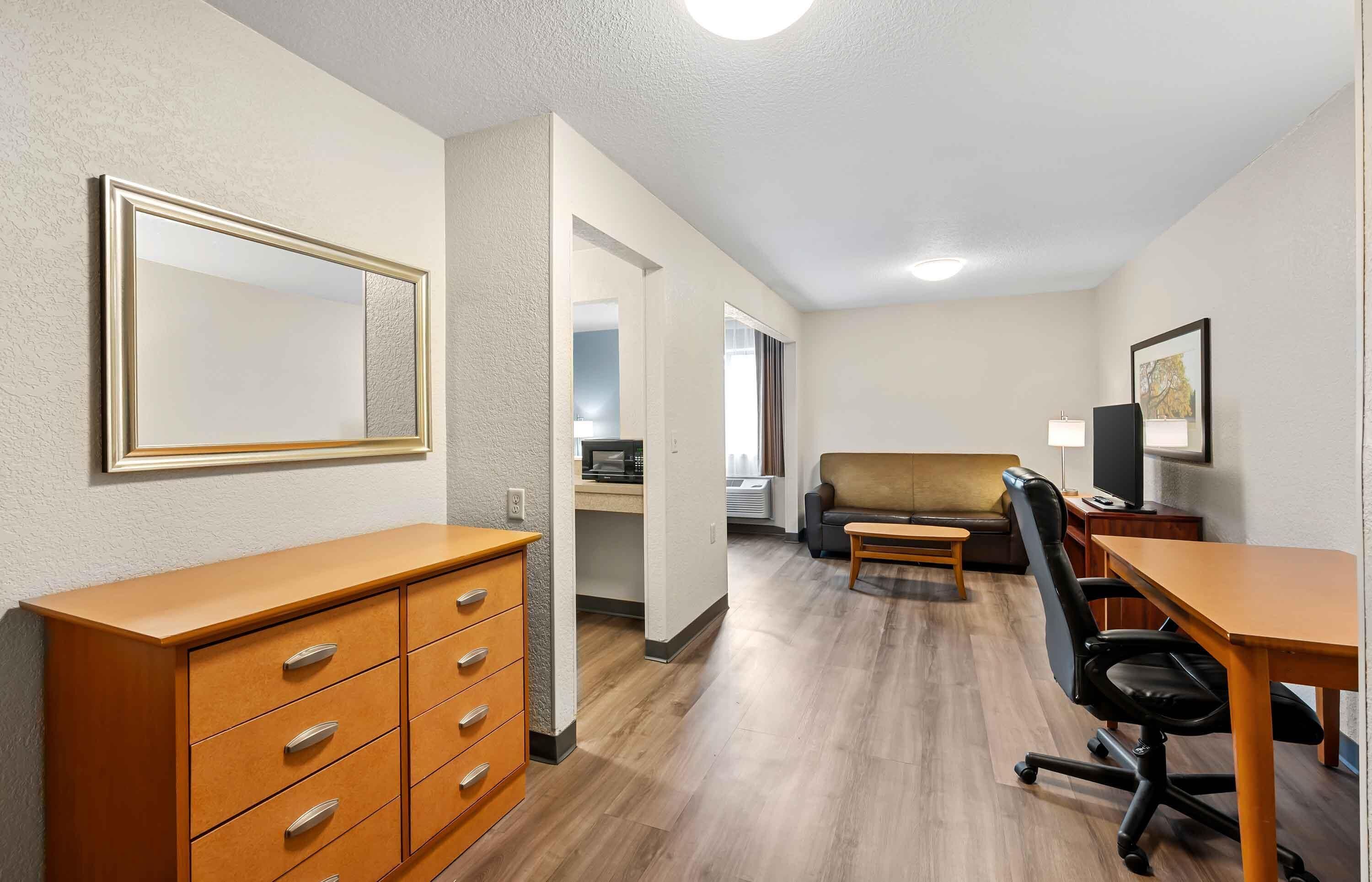 A compact living space with a kitchenette, a sofa, a desk with a chair, and a dresser.