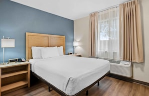 A hotel room with a bed, bedside tables, a lamp, a heater, and a window with curtains. - Extended Stay America Suites Fort Wayne North (Fort Wayne)