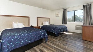 Habitación de hotel con dos camas, suelo de madera, un escritorio y una ventana con cortinas.