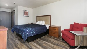 Un dormitorio con una cama, una mesita de noche, una silla roja y una pequeña mesa.
