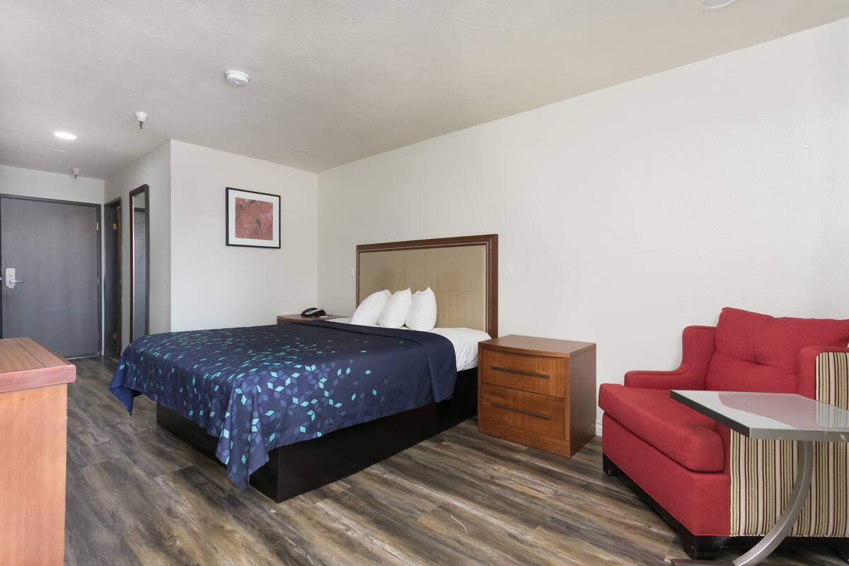 A bedroom with a bed, a nightstand, a red chair, and a small table.