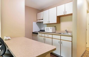 Cocina compacta con armarios blancos, microondas, estufa y lavaplatos.