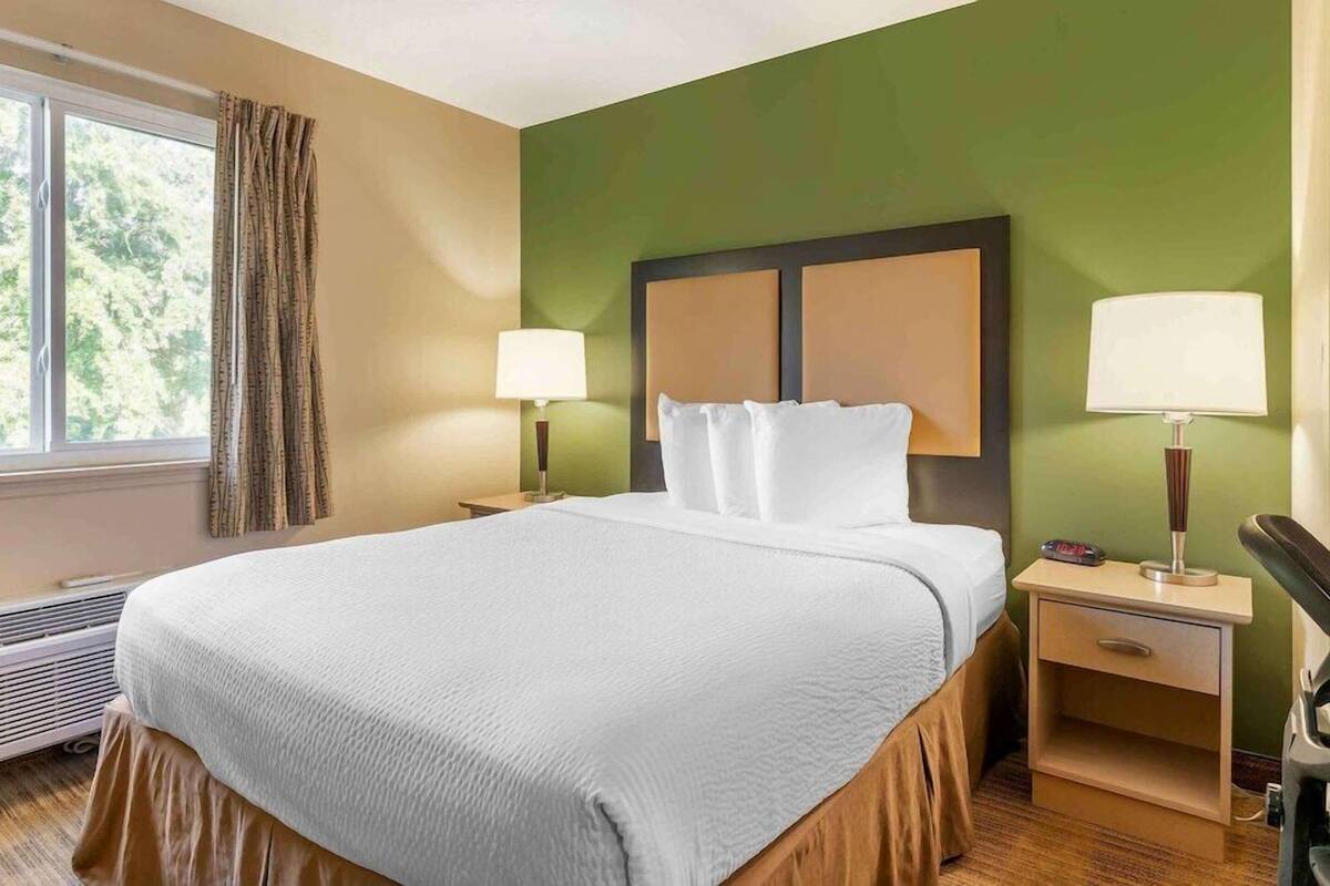 Habitación de hotel con una cama grande, dos mesitas de noche con lámparas, una ventana con cortinas y un radiador.