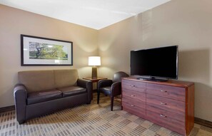 Habitación de hotel con sofá, televisión sobre un mueble de madera, lámpara y un cuadro en la pared.