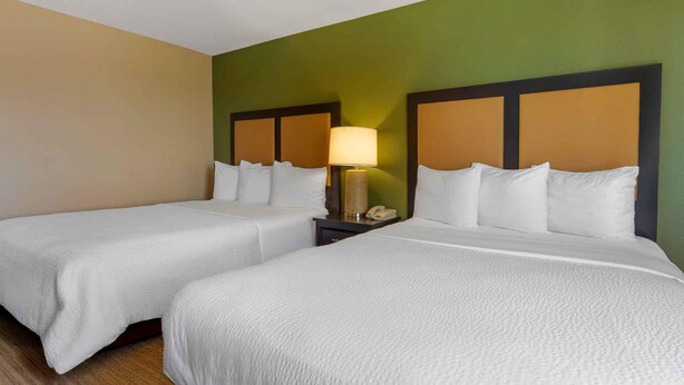 Habitación de hotel con dos camas, una mesita de noche con lámpara y una pared verde.