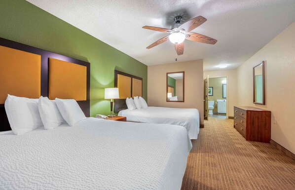 A hotel room with two beds, a ceiling fan, a mirror, a dresser, and a bathroom visible in the background.
