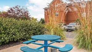 Una mesa azul al aire libre con cuatro sillas, un cubo de metal y un edificio de ladrillo al fondo.