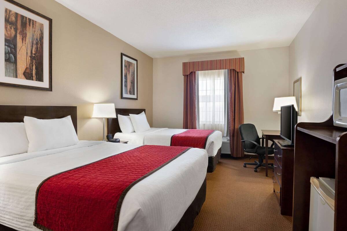 Quarto de hotel com duas camas, uma escrivaninha, uma cadeira e uma televisão.