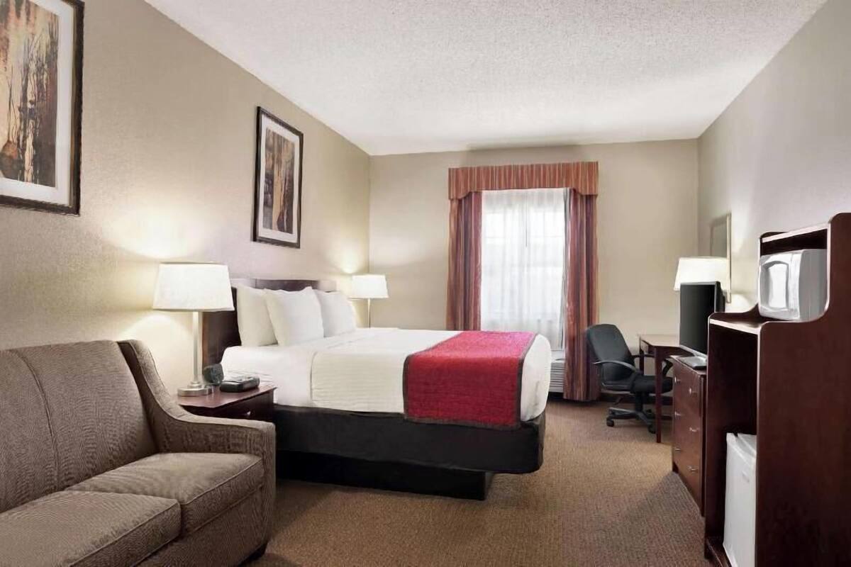Quarto de hotel com cama, escrivaninha, cadeira, televisão e sofá.