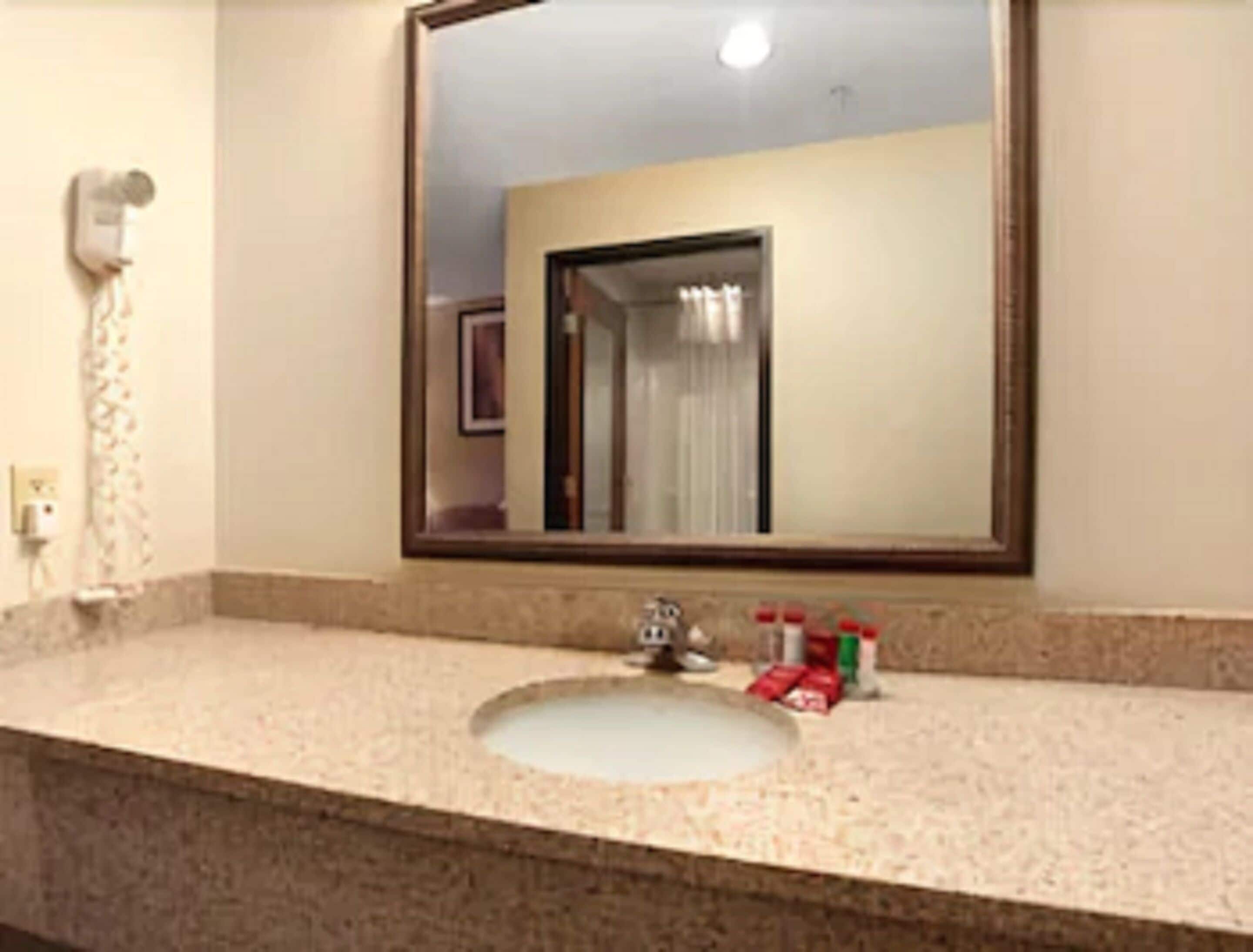 A bathroom with a sink, a mirror, and a towel dispenser.