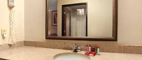 Un baño con lavamanos, espejo y dispensador de toallas.