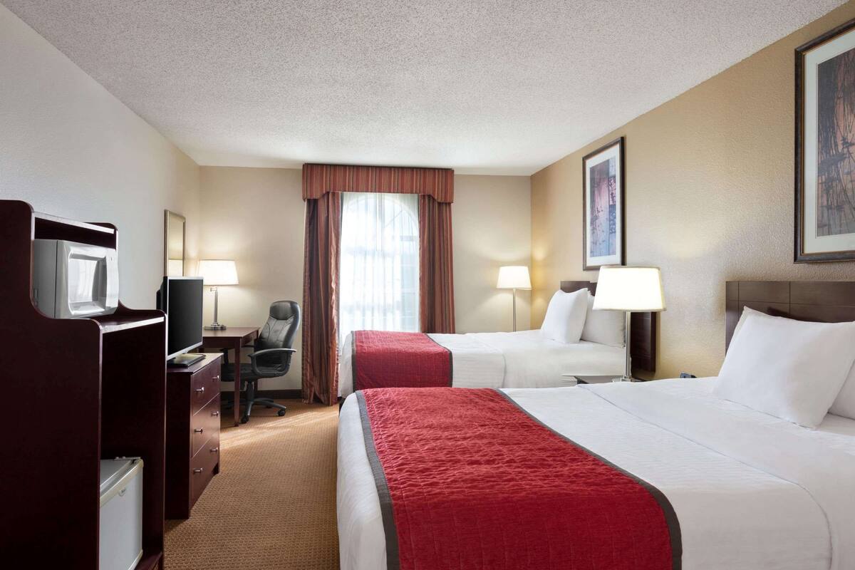 Quarto de hotel com duas camas, uma escrivaninha, uma cadeira, uma televisão e um abajur.